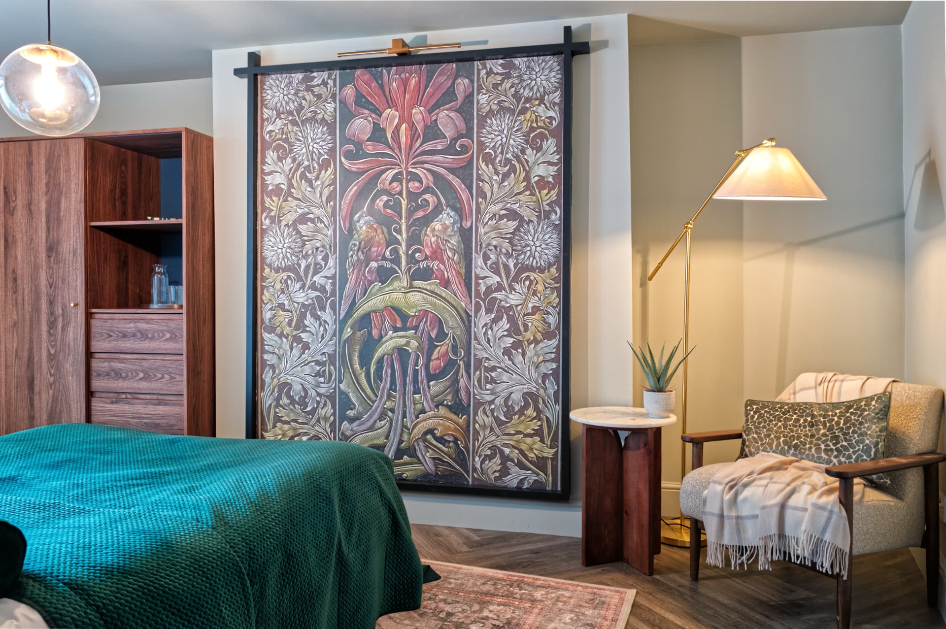 Spring suite bedroom at a Soulful Stays serviced apartment in Darlington, with a green knitted bed throw, a large decorative floral wall panel, a walnut wardrobe, brass floor lamp and a cushioned reading chair with a wool blanket